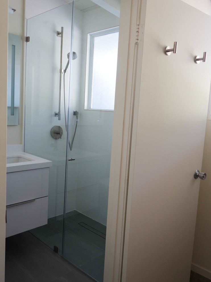Photo of a mid-sized midcentury 3/4 bathroom in San Francisco with flat-panel cabinets, white cabinets, an alcove shower, a two-piece toilet, white tile, porcelain tile, white walls, concrete floors, an undermount sink, engineered quartz benchtops, grey floor, a hinged shower door and white benchtops.