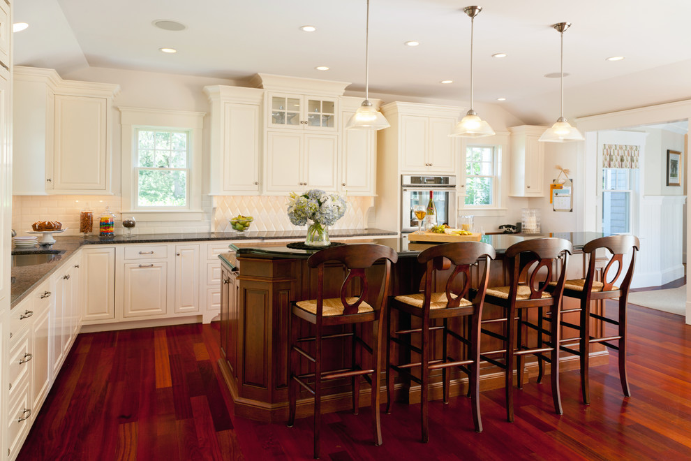 Inspiration for a transitional l-shaped medium tone wood floor eat-in kitchen remodel in Boston with an undermount sink, raised-panel cabinets, white cabinets, granite countertops, white backsplash, ceramic backsplash, stainless steel appliances and an island