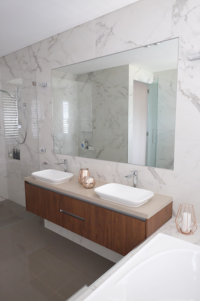 Design ideas for a mid-sized contemporary master bathroom in Sydney with recessed-panel cabinets, medium wood cabinets, a drop-in tub, a curbless shower, a wall-mount toilet, white tile, marble, white walls, ceramic floors, a vessel sink, engineered quartz benchtops, grey floor, an open shower and beige benchtops.