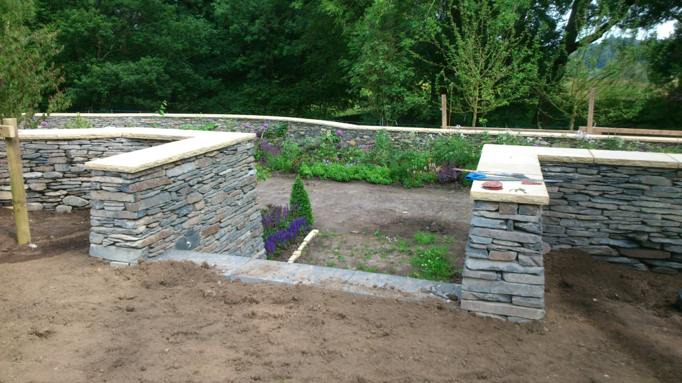 Foto de jardín clásico grande en patio trasero con jardín francés, muro de contención, adoquines de piedra natural y con piedra