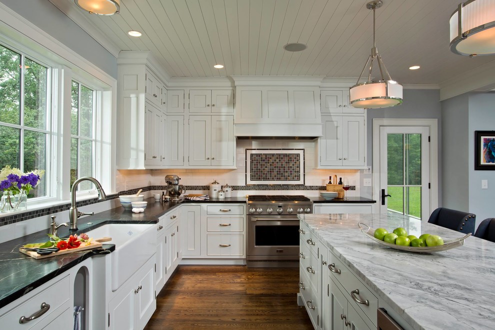 Inspiration for a large transitional l-shaped open plan kitchen in Boston with a farmhouse sink, shaker cabinets, white cabinets, brown splashback, mosaic tile splashback, dark hardwood floors, with island, brown floor, stainless steel appliances and marble benchtops.