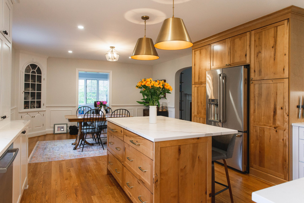 Large transitional l-shaped eat-in kitchen in Baltimore with an undermount sink, shaker cabinets, white cabinets, quartz benchtops, white splashback, marble splashback, stainless steel appliances, medium hardwood floors, with island, brown floor and white benchtop.