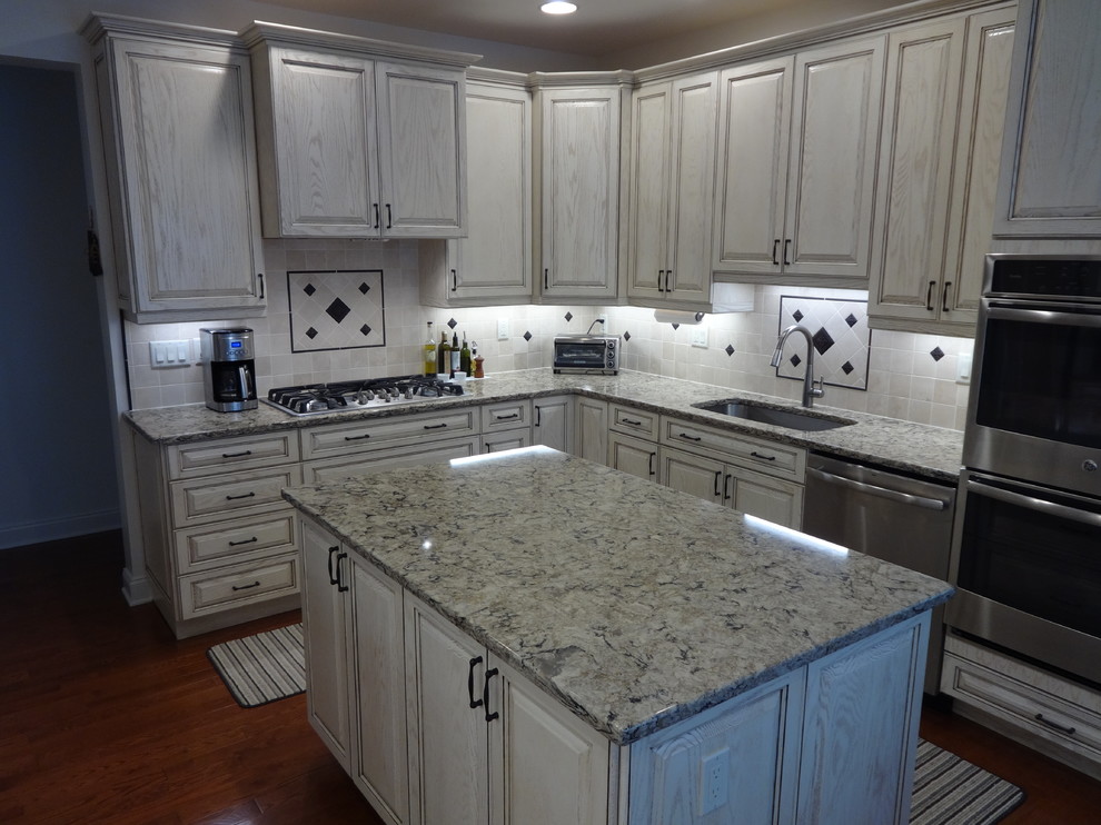 This is an example of an expansive country u-shaped eat-in kitchen in New York with raised-panel cabinets, distressed cabinets, quartz benchtops, stainless steel appliances, dark hardwood floors, with island and multi-coloured benchtop.