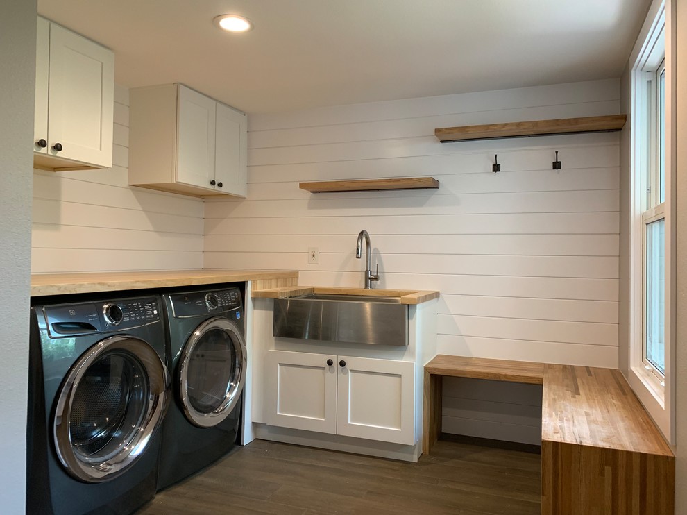 Photo of a mid-sized country u-shaped utility room in Denver with a farmhouse sink, recessed-panel cabinets, white cabinets, wood benchtops, white walls, a side-by-side washer and dryer, brown floor, vinyl floors and beige benchtop.