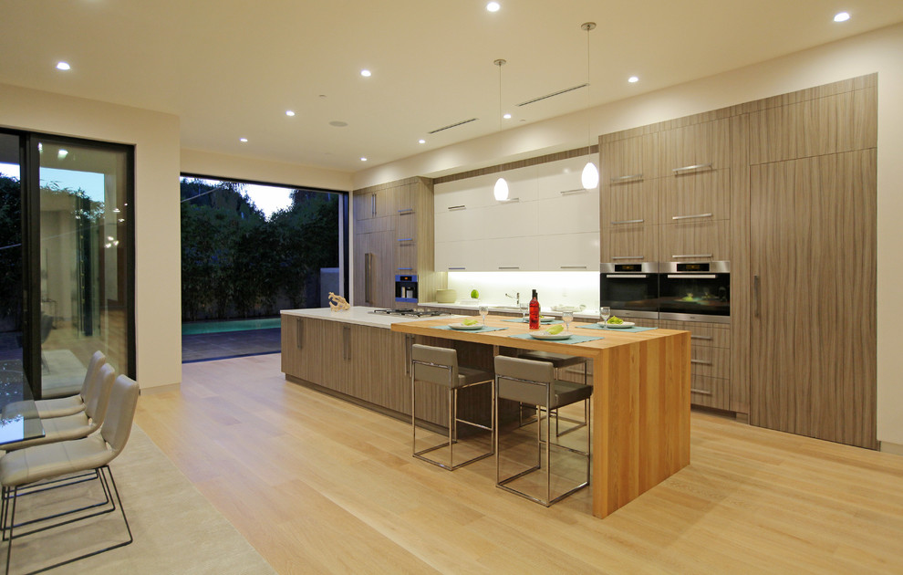 This is an example of a contemporary galley eat-in kitchen in Los Angeles with an undermount sink, flat-panel cabinets, medium wood cabinets, wood benchtops, white splashback, glass sheet splashback and stainless steel appliances.