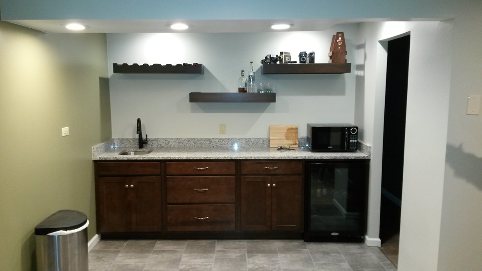 This is an example of a small modern single-wall wet bar in Philadelphia with an undermount sink, recessed-panel cabinets, dark wood cabinets, granite benchtops, multi-coloured splashback, stone slab splashback, grey floor and multi-coloured benchtop.