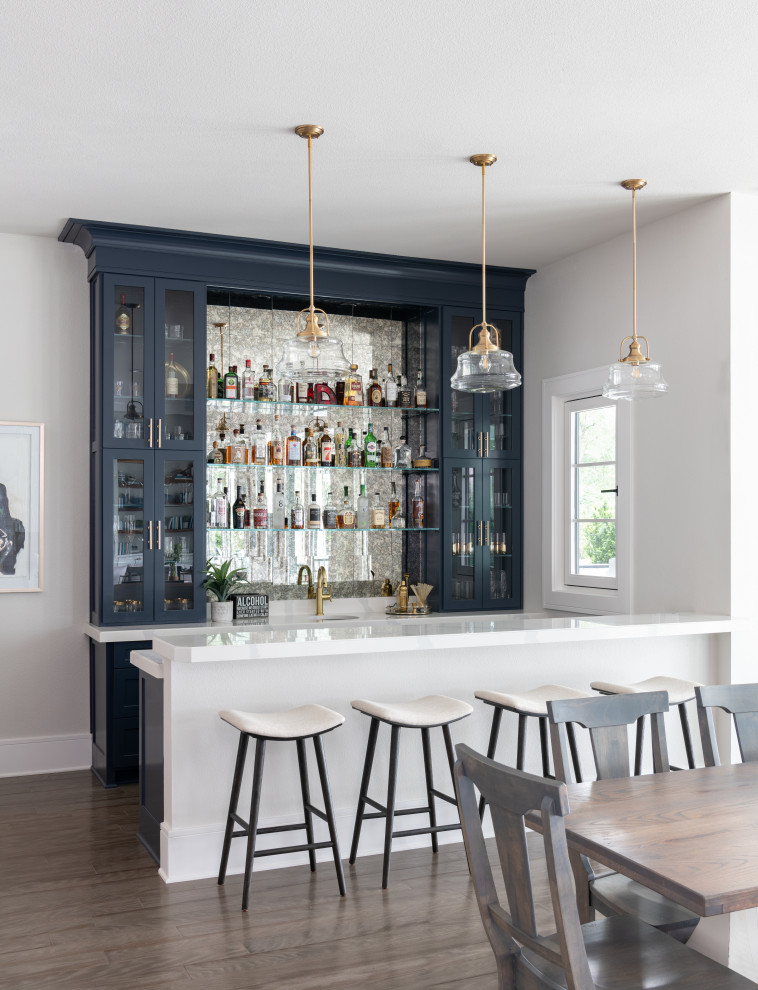 Photo of a large nautical galley wet bar in Dallas with a submerged sink, glass-front cabinets, blue cabinets, engineered stone countertops, grey splashback, mirror splashback, porcelain flooring, brown floors and white worktops.