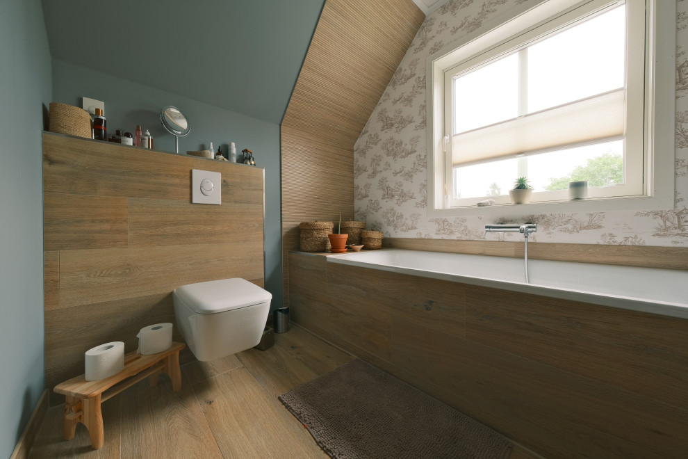 Mid-sized scandinavian 3/4 bathroom in Berlin with a drop-in tub, a curbless shower, a wall-mount toilet, brown tile, ceramic tile, green walls, wood-look tile, brown floor, a sliding shower screen, a built-in vanity, wallpaper and wallpaper.