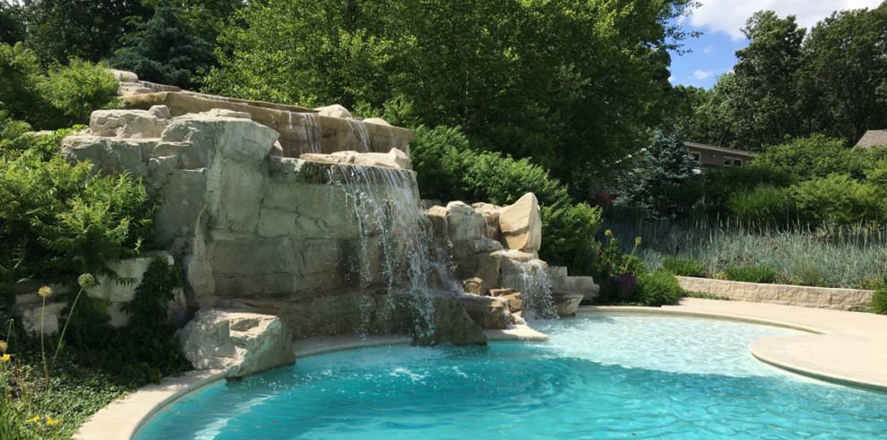 Inspiration for a mid-sized traditional backyard custom-shaped lap pool in Cedar Rapids with a water feature and natural stone pavers.