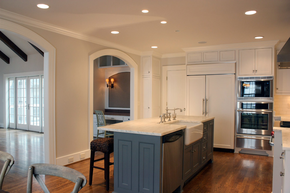 Large traditional u-shaped eat-in kitchen in Nashville with a farmhouse sink, raised-panel cabinets, white cabinets, marble benchtops, white splashback, subway tile splashback, stainless steel appliances, dark hardwood floors and with island.
