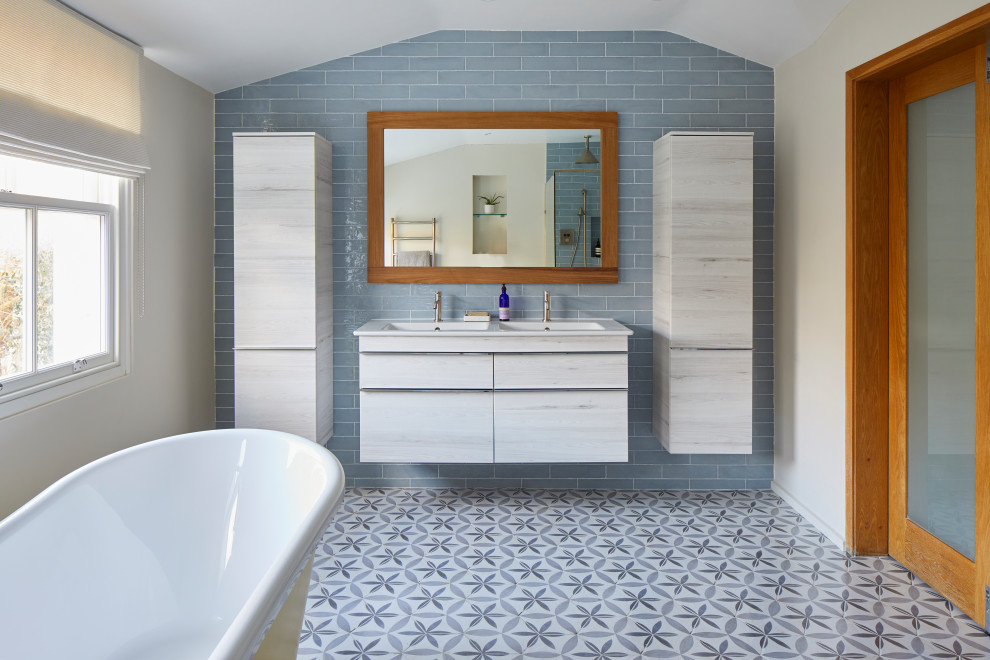 This is an example of a large contemporary family bathroom in London with white cabinets, a freestanding bath, a walk-in shower, a wall mounted toilet, blue tiles, an integrated sink, an open shower, double sinks and a floating vanity unit.