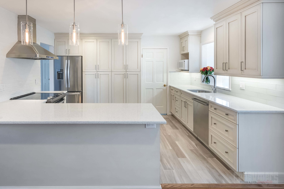 Photo of a mid-sized u-shaped eat-in kitchen in New York with an undermount sink, recessed-panel cabinets, white cabinets, stainless steel appliances, plywood floors and a peninsula.