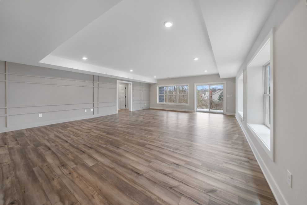 Example of a large transitional walk-out tray ceiling and wall paneling basement design in Cincinnati with a bar