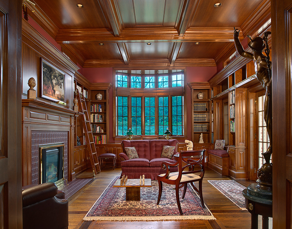 Photo of a large traditional enclosed living room in DC Metro with a library, brown walls, medium hardwood floors, a standard fireplace, a tile fireplace surround and no tv.