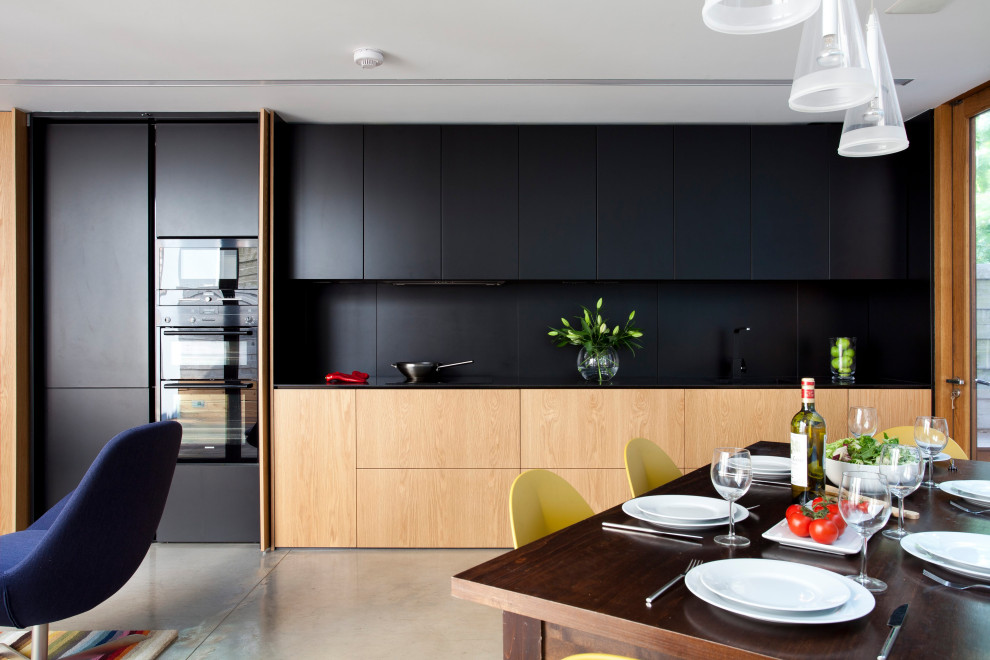 This is an example of a contemporary single-wall open plan kitchen in Dublin with flat-panel cabinets, black cabinets, black splashback, concrete flooring and grey floors.