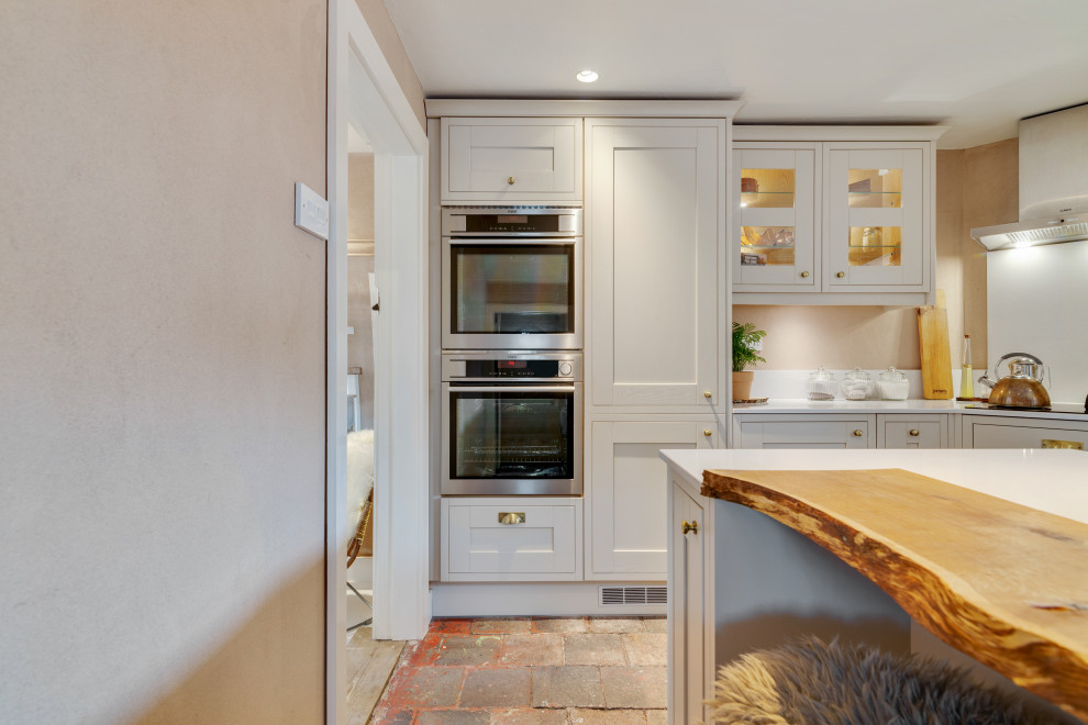 Design ideas for a small transitional u-shaped separate kitchen in Cheshire with an undermount sink, shaker cabinets, green cabinets, quartz benchtops, white splashback, engineered quartz splashback, stainless steel appliances, brick floors, a peninsula, multi-coloured floor and white benchtop.