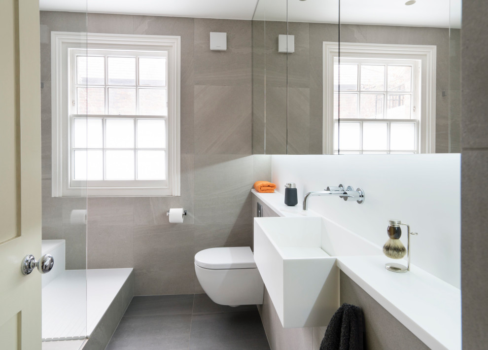 Mid-sized contemporary kids bathroom in London with a wall-mount toilet, beige walls, a wall-mount sink, grey floor, an open shower, a drop-in tub and a single vanity.