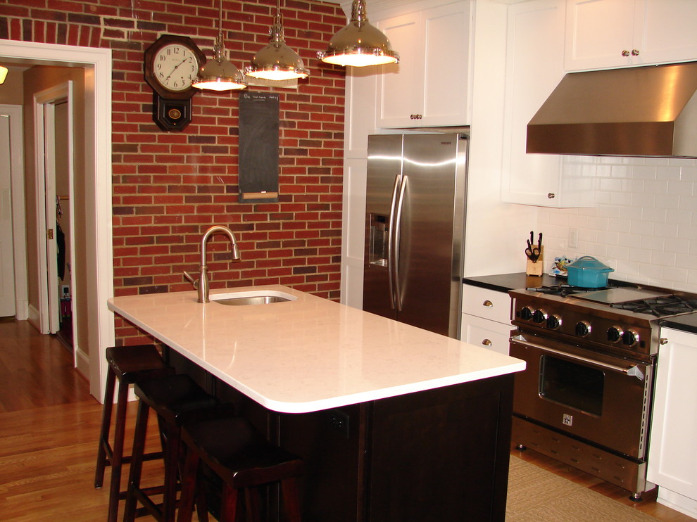 Photo of a mid-sized transitional l-shaped eat-in kitchen in DC Metro with an undermount sink, white cabinets, granite benchtops, white splashback, ceramic splashback, stainless steel appliances, light hardwood floors and with island.