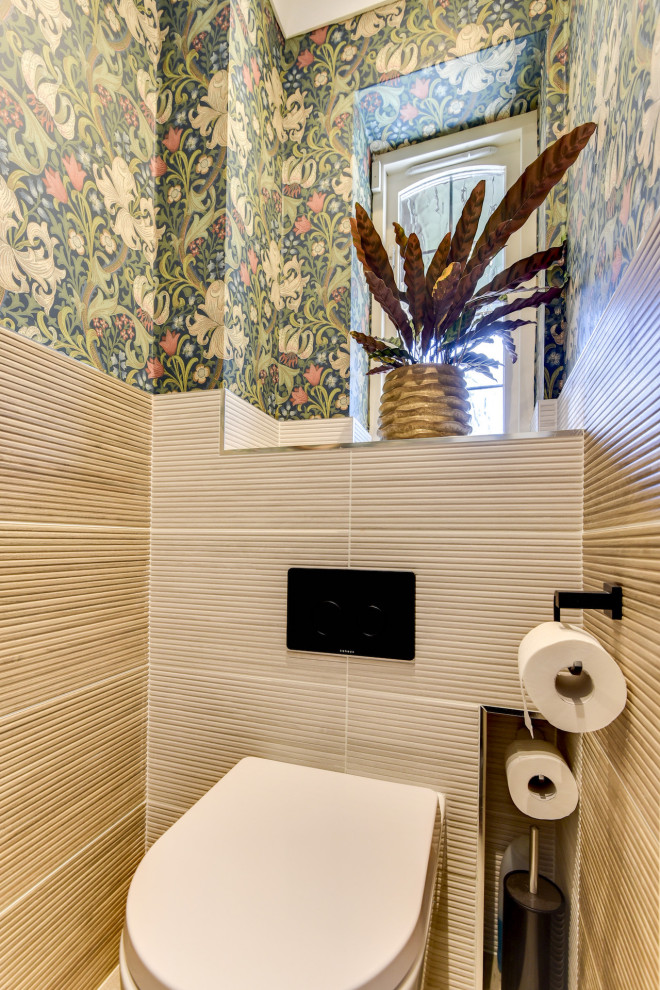Small modern powder room in Sussex with a one-piece toilet, beige tile, ceramic tile, multi-coloured walls, ceramic floors, a wall-mount sink, tile benchtops, beige floor, beige benchtops and wallpaper.