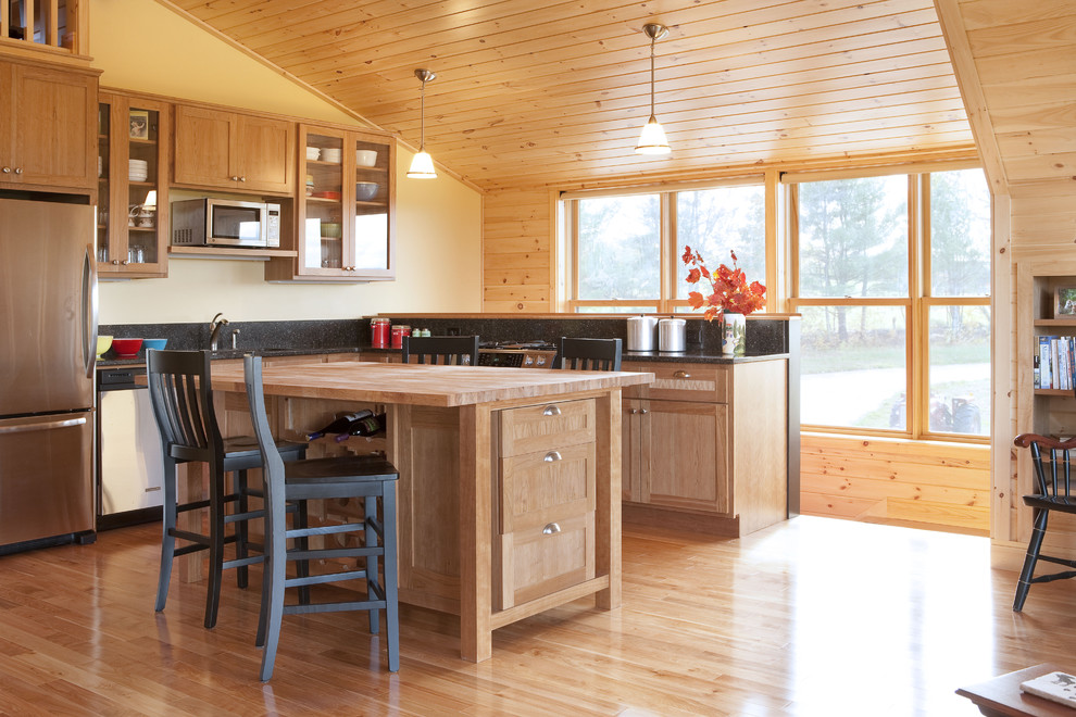 Design ideas for a mid-sized country l-shaped eat-in kitchen in Portland Maine with stainless steel appliances, wood benchtops, a drop-in sink, recessed-panel cabinets, light wood cabinets, black splashback, stone slab splashback, light hardwood floors and with island.