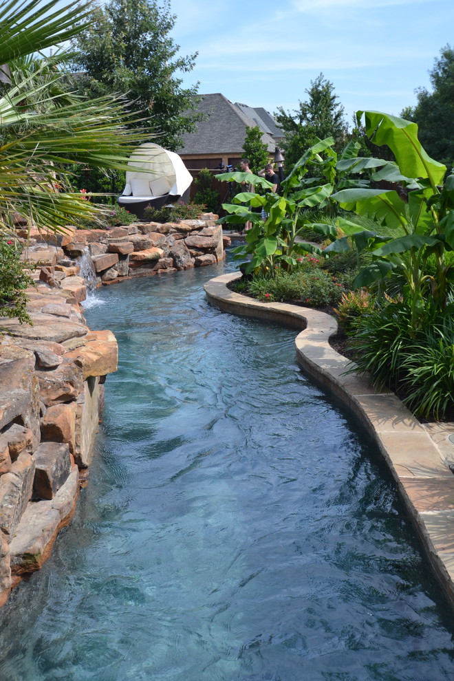 Design ideas for a large tropical backyard custom-shaped natural pool in Dallas with a water feature and natural stone pavers.
