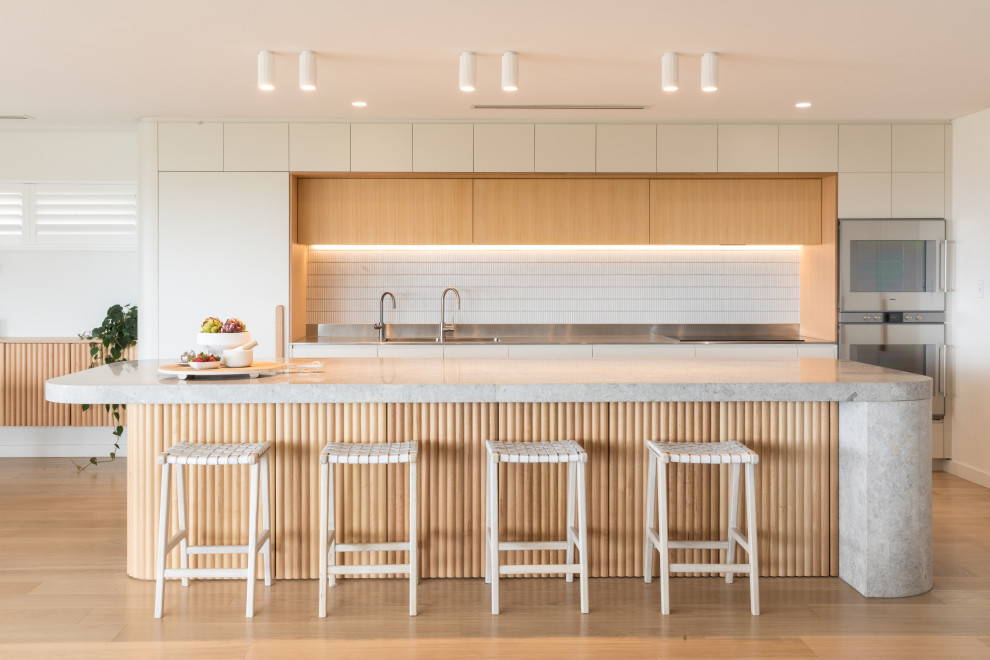 Modern inredning av ett stort grå grått kök, med en integrerad diskho, vita skåp, bänkskiva i kalksten, vitt stänkskydd, stänkskydd i cementkakel, integrerade vitvaror, ljust trägolv, en köksö och beiget golv
