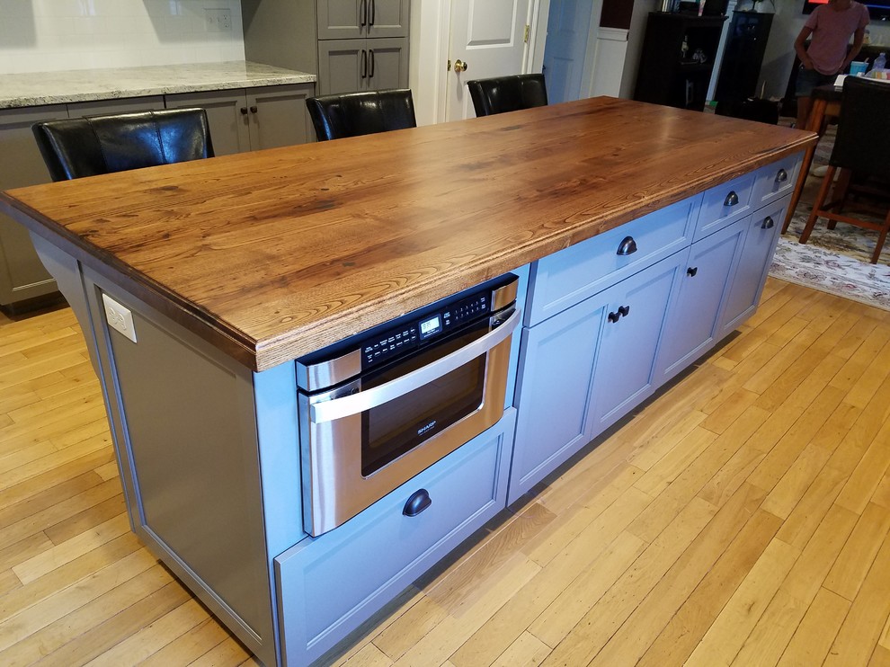 Mid-sized transitional galley light wood floor and brown floor eat-in kitchen photo with a farmhouse sink, recessed-panel cabinets, gray cabinets, wood countertops, white backsplash, subway tile backsplash, stainless steel appliances and an island