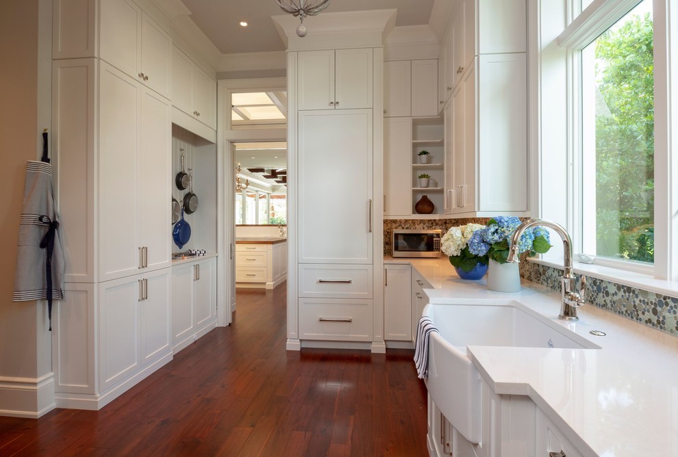 Mid-sized tropical galley utility room in Miami with a farmhouse sink, raised-panel cabinets, white cabinets, quartzite benchtops, white walls, medium hardwood floors, a side-by-side washer and dryer, brown floor and white benchtop.