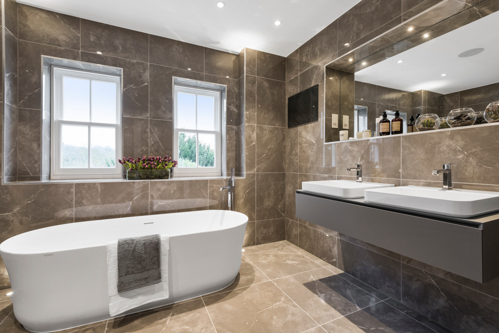 Contemporary master bathroom in London with flat-panel cabinets, grey cabinets, a freestanding tub, gray tile, a vessel sink and grey floor.