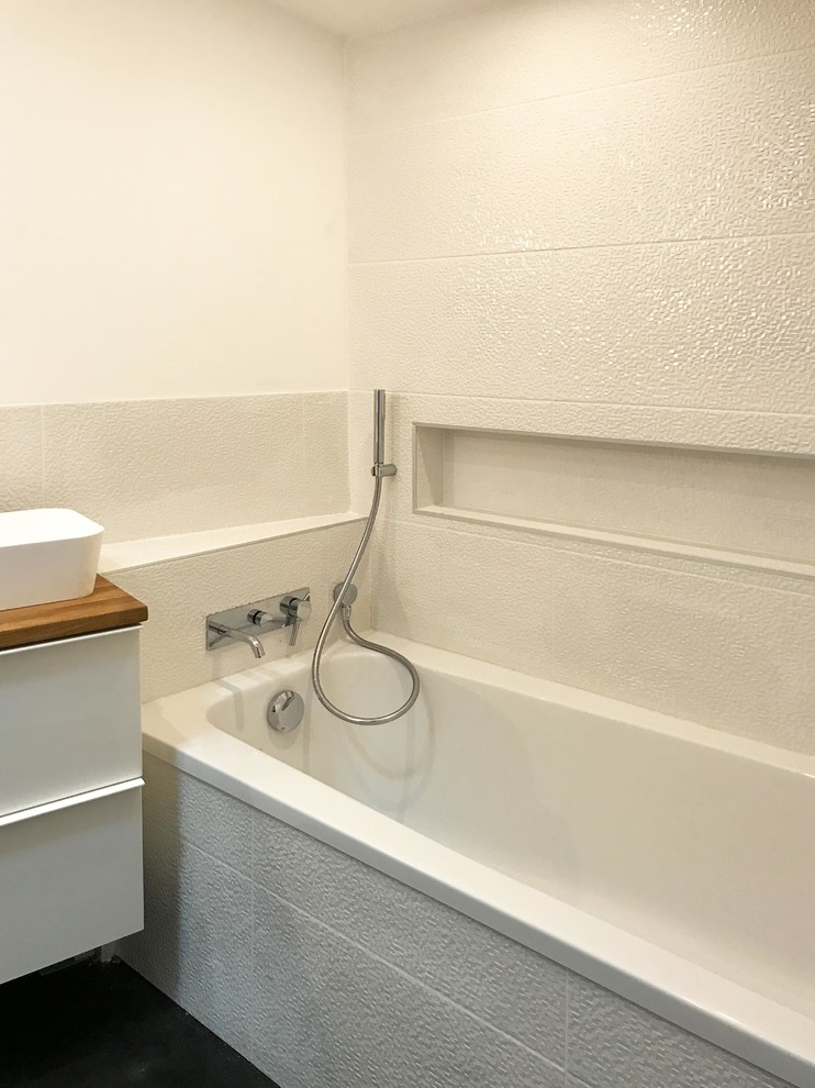 Cette image montre une salle de bain principale design de taille moyenne avec une baignoire encastrée, une douche à l'italienne, un carrelage blanc, un mur blanc, un sol en vinyl, un lavabo posé, un plan de toilette en bois, un sol noir et aucune cabine.