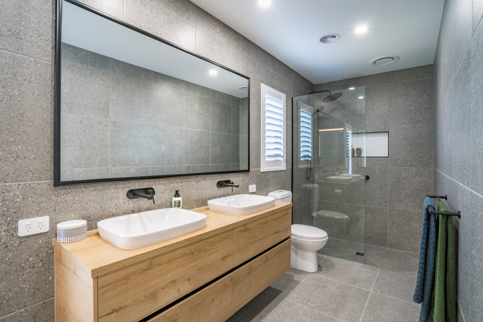 Inspiration for a mid-sized contemporary master bathroom in Other with flat-panel cabinets, light wood cabinets, an open shower, a one-piece toilet, gray tile, ceramic tile, grey walls, ceramic floors, laminate benchtops, grey floor, an open shower, brown benchtops, a double vanity and a floating vanity.