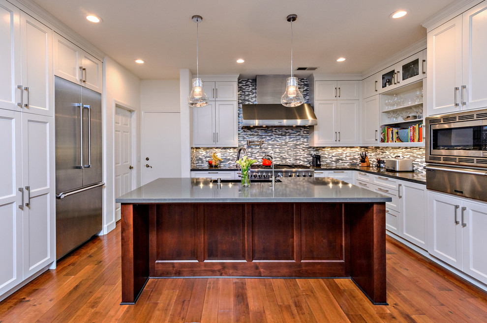 Example of a transitional u-shaped medium tone wood floor enclosed kitchen design in San Diego with shaker cabinets, white cabinets, multicolored backsplash, mosaic tile backsplash, stainless steel appliances, white walls and an island