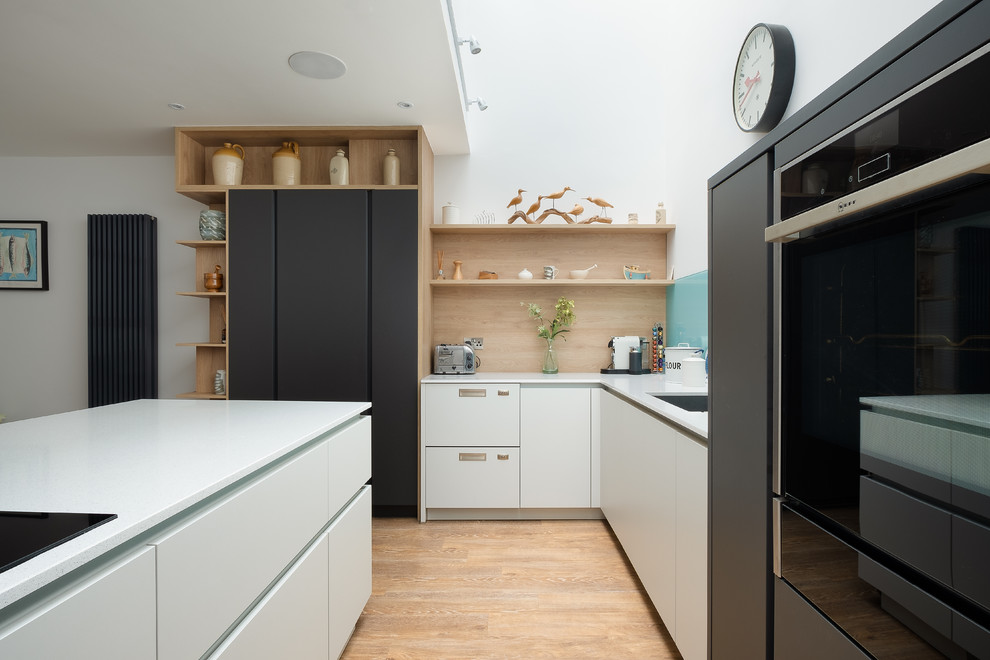 Diseño de cocina comedor actual de tamaño medio sin isla con armarios con paneles lisos, puertas de armario grises, encimera de cuarcita, salpicadero azul, salpicadero de vidrio templado, electrodomésticos negros, suelo de madera en tonos medios y encimeras blancas