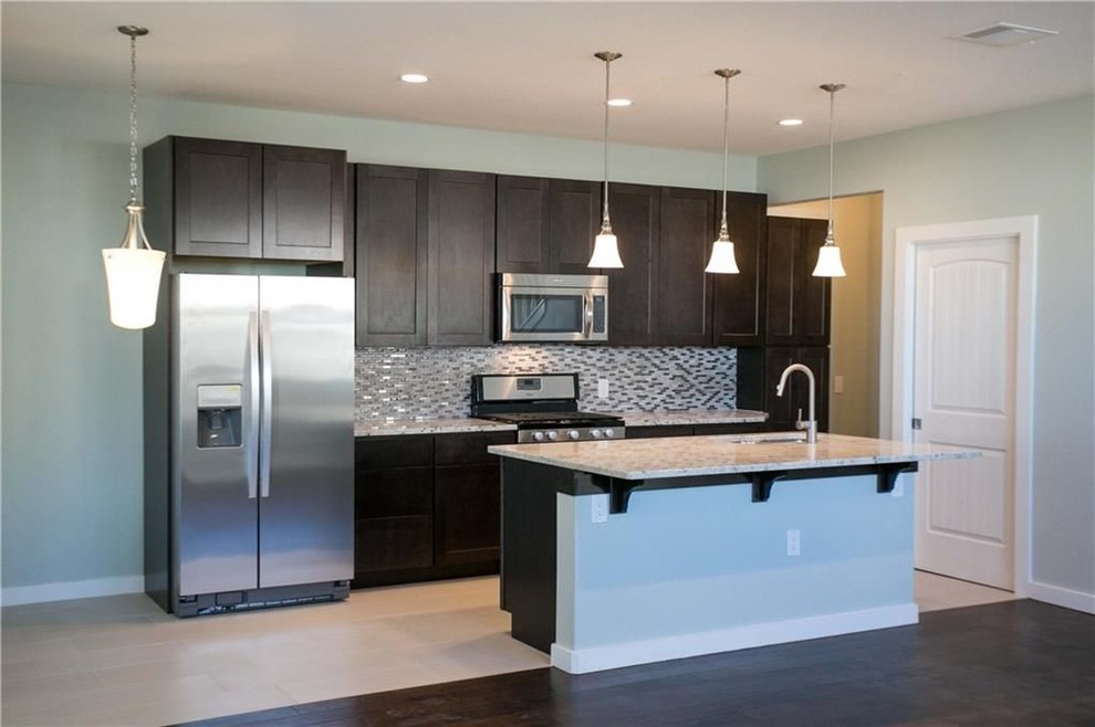 Inspiration for a mid-sized transitional single-wall porcelain tile and beige floor eat-in kitchen remodel in Austin with a double-bowl sink, shaker cabinets, dark wood cabinets, granite countertops, gray backsplash, mosaic tile backsplash, stainless steel appliances, an island and gray countertops
