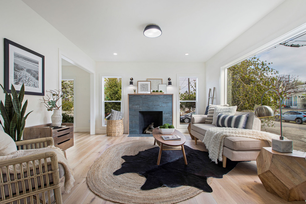 This is an example of a small scandinavian formal enclosed living room in San Francisco with white walls, light hardwood floors, a standard fireplace, a wood fireplace surround and no tv.