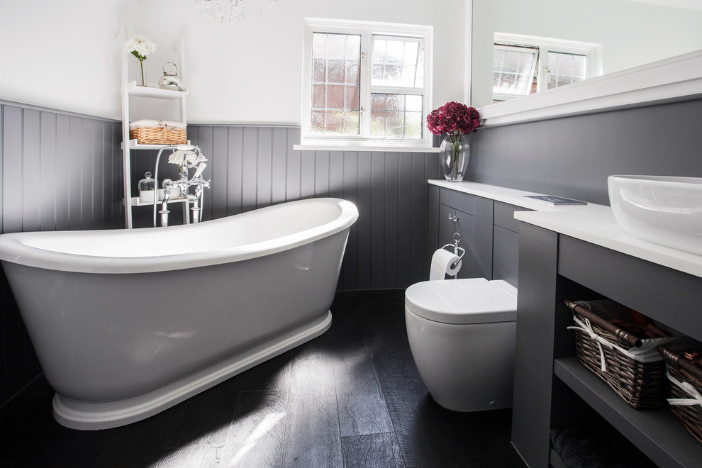 This is an example of a mid-sized contemporary kids bathroom in Kent with flat-panel cabinets, grey cabinets, a freestanding tub, a corner shower, a wall-mount toilet, black and white tile, white walls, dark hardwood floors, a drop-in sink, quartzite benchtops, an open shower and white benchtops.