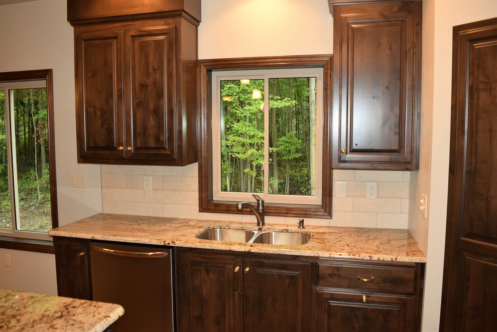 Inspiration for a light wood floor open concept kitchen remodel with an undermount sink, raised-panel cabinets, dark wood cabinets, granite countertops, white backsplash, ceramic backsplash, stainless steel appliances and a peninsula