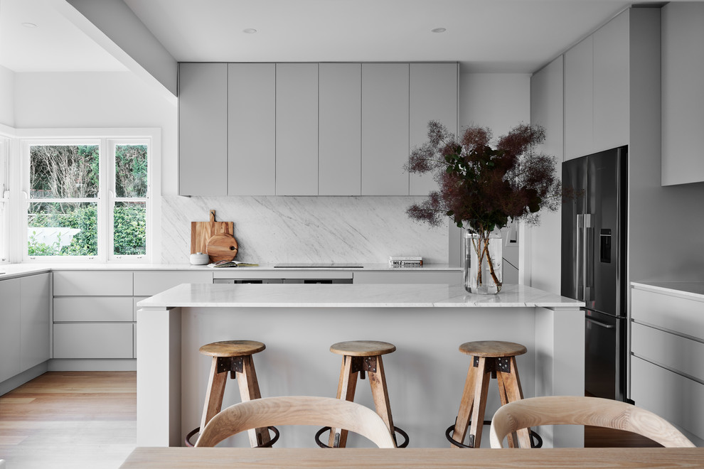 Inspiration for a large contemporary u-shaped eat-in kitchen in Wollongong with grey cabinets, marble benchtops, marble splashback, stainless steel appliances, with island, flat-panel cabinets, white splashback, medium hardwood floors, brown floor, white benchtop and a double-bowl sink.