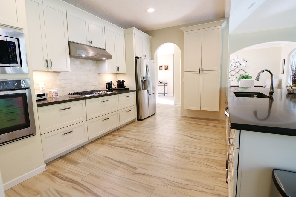 Mid-sized transitional u-shaped porcelain tile and beige floor eat-in kitchen photo in Houston with an undermount sink, recessed-panel cabinets, white cabinets, soapstone countertops, white backsplash, subway tile backsplash, stainless steel appliances, an island and black countertops