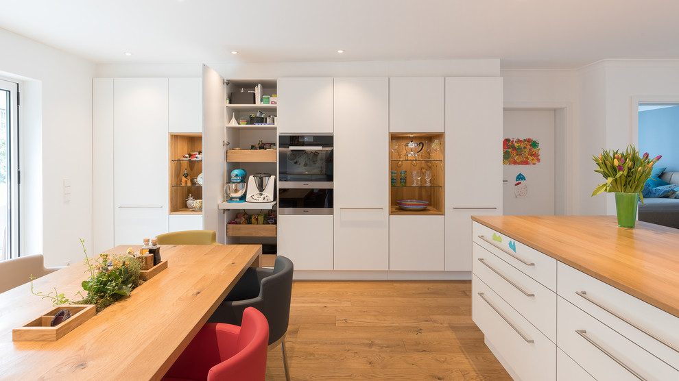 Inspiration for a large contemporary galley eat-in kitchen in Stuttgart with a double-bowl sink, flat-panel cabinets, white cabinets, wood benchtops, white splashback, stainless steel appliances, medium hardwood floors, brown floor, brown benchtop and with island.