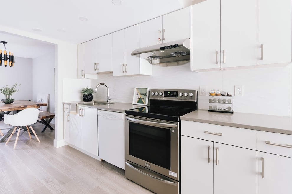 Photo of a mid-sized modern single-wall eat-in kitchen in Vancouver with a drop-in sink, flat-panel cabinets, white cabinets, solid surface benchtops, white splashback, stone tile splashback, plywood floors, no island, brown floor and brown benchtop.