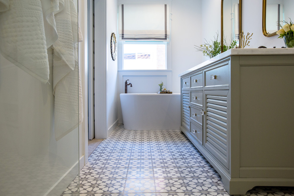 This is an example of a mid-sized country master bathroom in Los Angeles with louvered cabinets, grey cabinets, a freestanding tub, an alcove shower, a one-piece toilet, white tile, ceramic tile, white walls, cement tiles, an undermount sink, marble benchtops, grey floor and a hinged shower door.