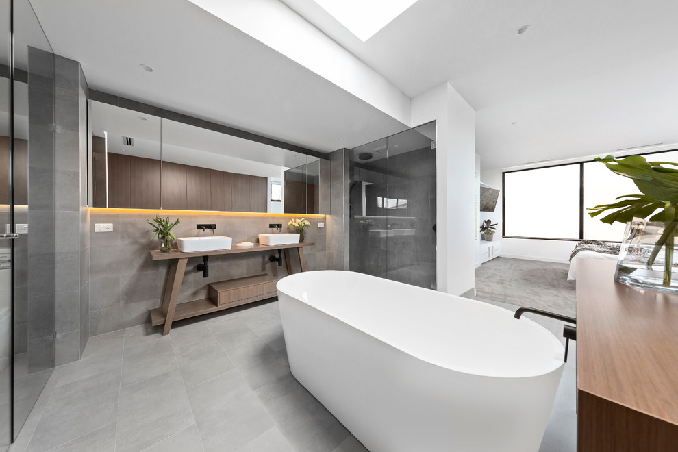 This is an example of a contemporary master bathroom in Melbourne with a freestanding tub, an alcove shower, gray tile, grey walls, a vessel sink and wood benchtops.