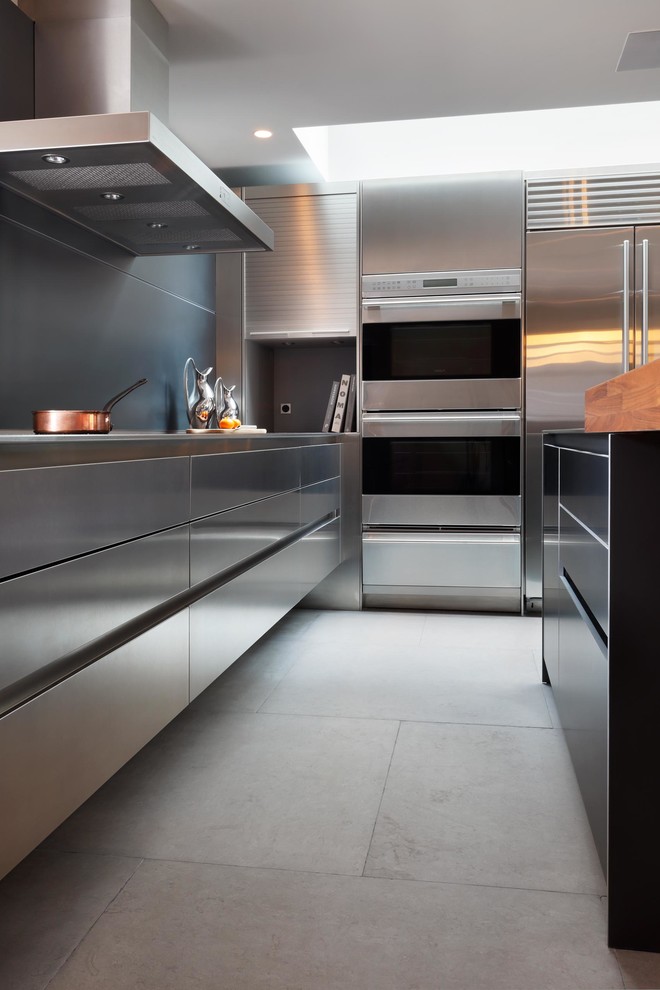 Design ideas for a mid-sized contemporary l-shaped eat-in kitchen in London with an integrated sink, flat-panel cabinets, stainless steel cabinets, stainless steel benchtops, metallic splashback, stainless steel appliances, limestone floors and with island.
