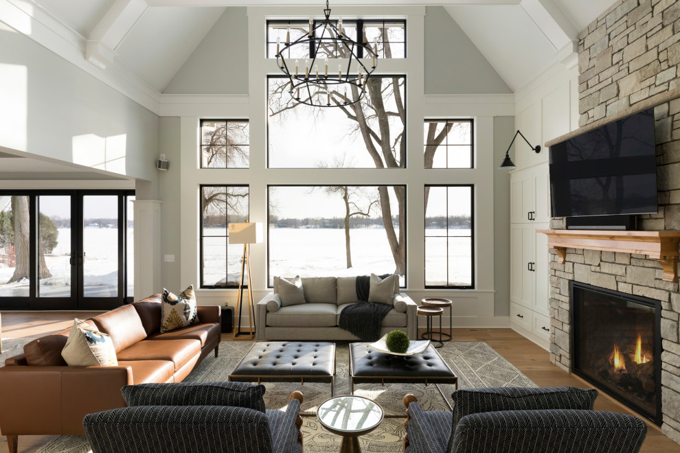 Стильный дизайн: большая открытая гостиная комната в стиле неоклассика (современная классика) с серыми стенами, светлым паркетным полом, стандартным камином, фасадом камина из камня и сводчатым потолком - последний тренд