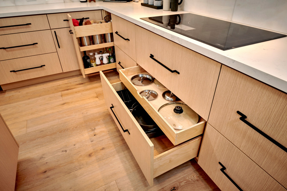 Exemple d'une cuisine moderne en L et bois clair fermée et de taille moyenne avec un placard à porte plane, un plan de travail en quartz modifié, un électroménager en acier inoxydable, parquet clair, un sol marron et un plan de travail blanc.