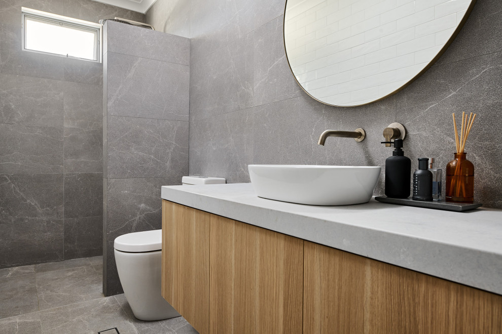 Design ideas for a mid-sized powder room in Perth with furniture-like cabinets, light wood cabinets, a one-piece toilet, gray tile, ceramic tile, white walls, ceramic floors, a vessel sink, engineered quartz benchtops, grey floor, grey benchtops and a floating vanity.