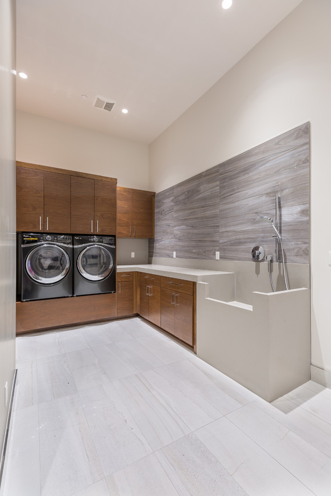 Design ideas for a mid-sized contemporary l-shaped dedicated laundry room in Las Vegas with an integrated sink, flat-panel cabinets, medium wood cabinets, solid surface benchtops, grey walls, ceramic floors and a side-by-side washer and dryer.