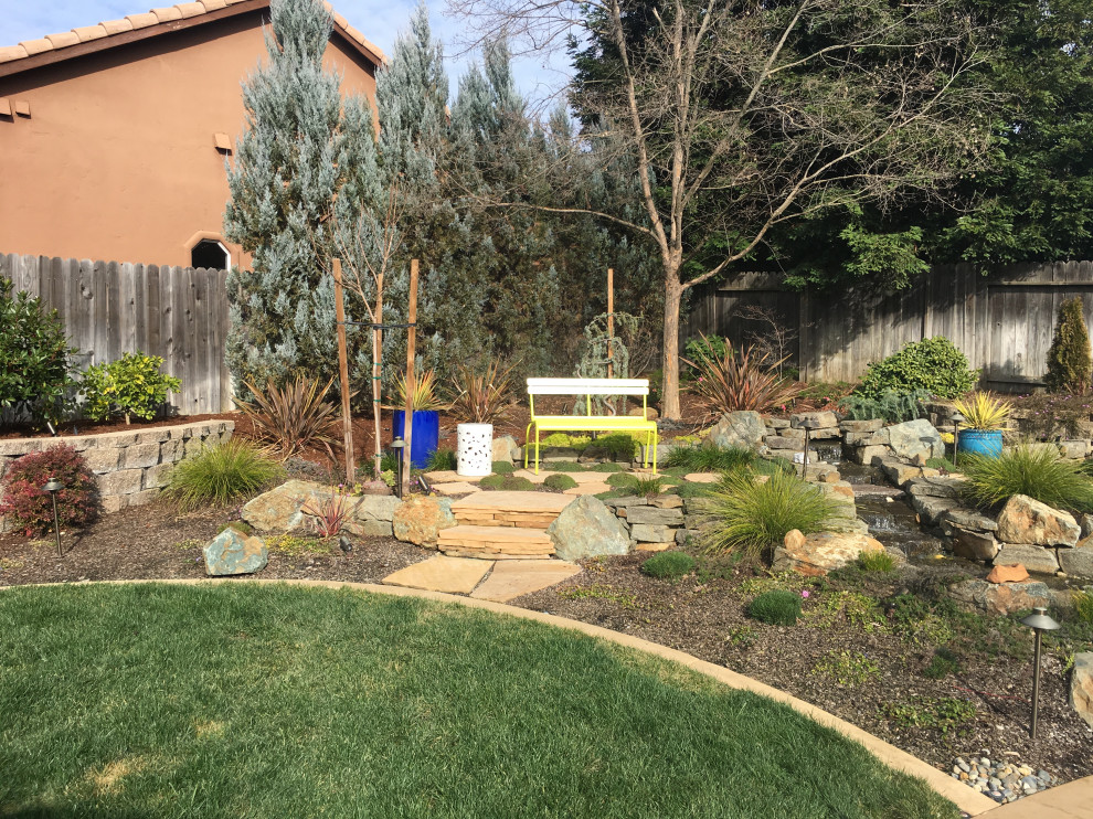 Photo of a mediterranean back xeriscape full sun garden for summer in Sacramento with a rockery and natural stone paving.