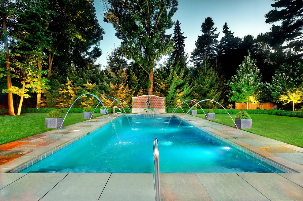 This is an example of a mid-sized traditional backyard rectangular pool in Chicago with a water feature and natural stone pavers.
